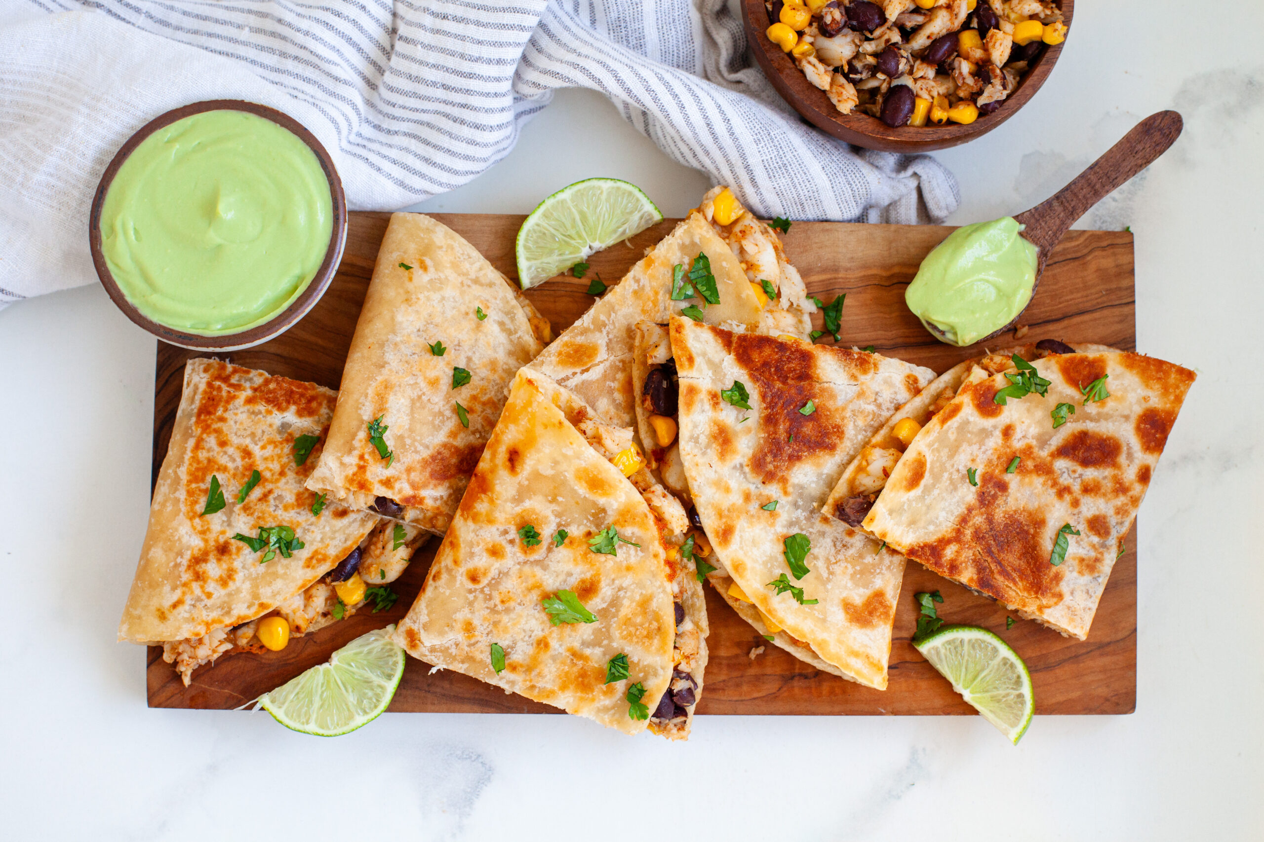 Crispy Alaska sole quesadillas cut into wedges, served with avocado crema dip on a wooden board.