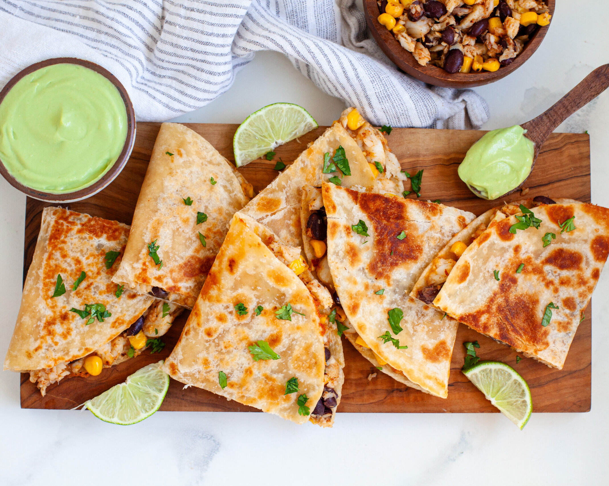 Crispy Alaska sole quesadillas cut into wedges, served with avocado crema dip on a wooden board.